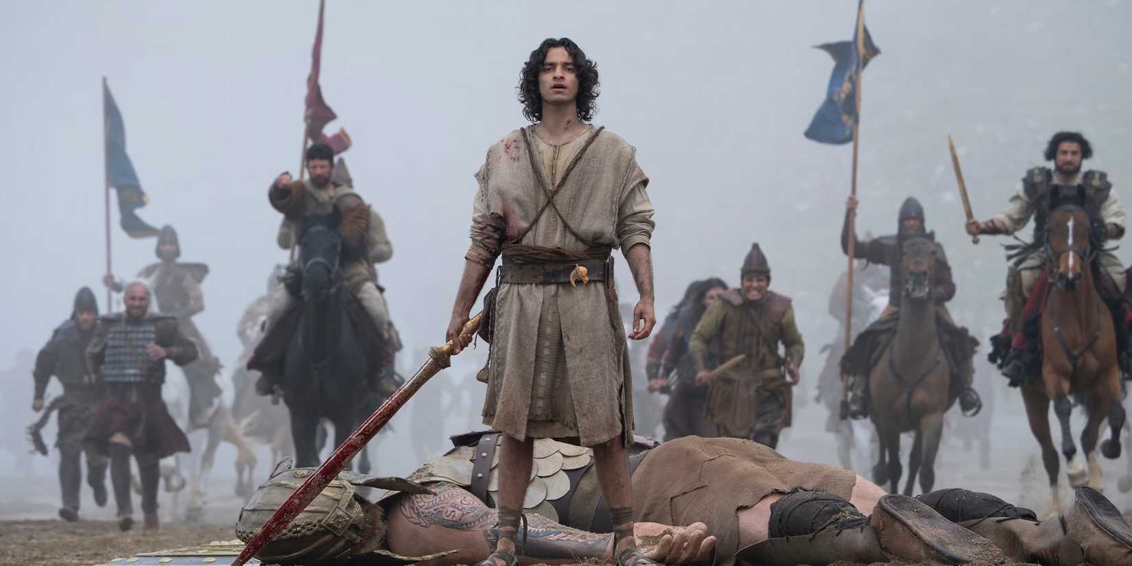 David (Michael Iskander) sobre o corpo de Golias enquanto guerreiros se aproximam em "House of David"