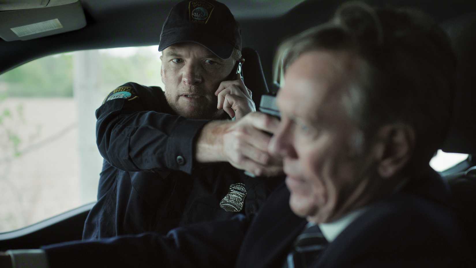 Sam Worthington como David aponta arma para alguém enquanto fala ao telefone no carro em I Will Find